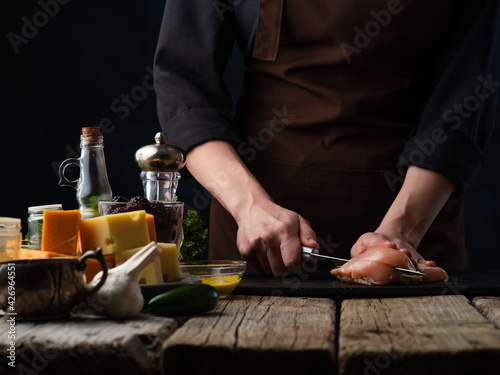 Chef cuts chicken fillet on the background of food.Cooking meat, and recipes with chicken.Culinary recipes and cooking.Concept of a book of recipes and menus for restaurants, hotels and cafes