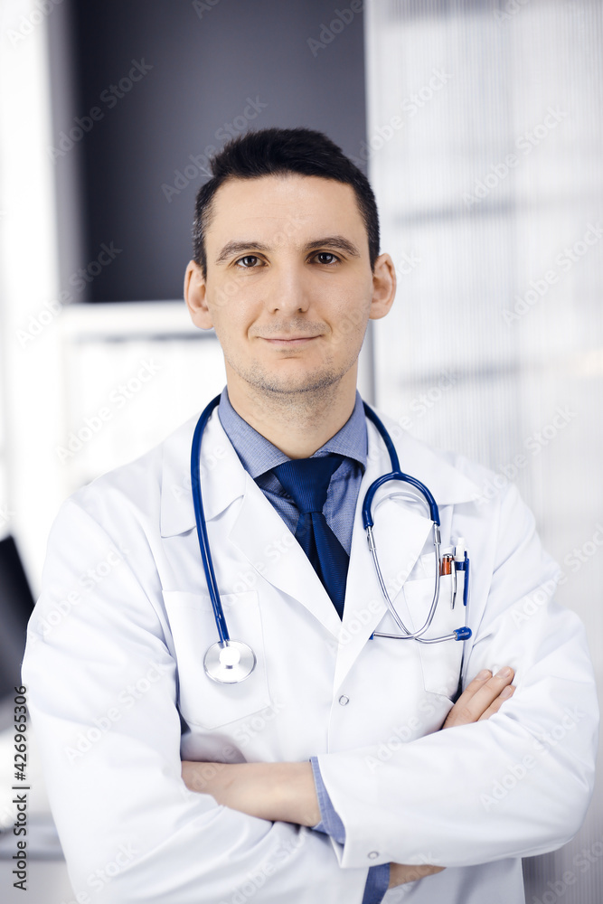 Male doctor standing straight with arms crossed in clinic near his working place. Perfect medical service in hospital. Medicine and healthcare concept Male doctor standing straight with arms crossed in clinic near his working place. Perfect medical service in hospital. Medicine and healthcare concept