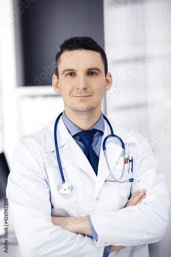Male doctor standing straight with arms crossed in clinic near his working place. Perfect medical service in hospital. Medicine and healthcare concept