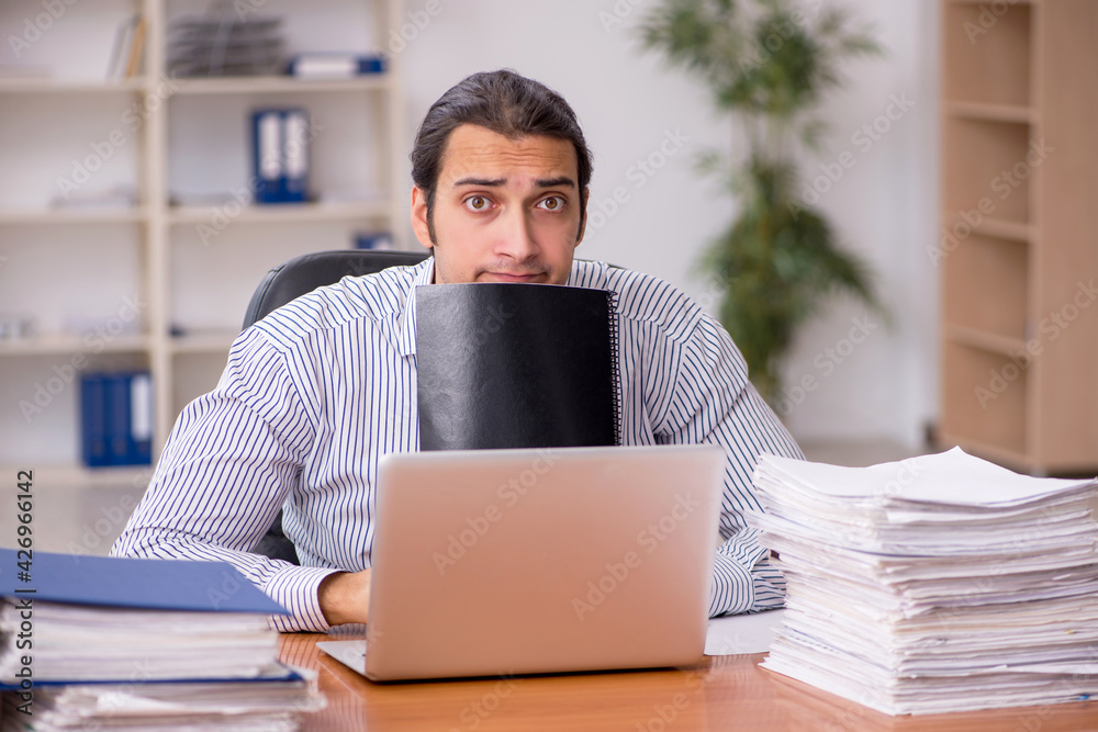 Young male employee unhappy with excessive work in the office Young male employee unhappy with excessive work in the office