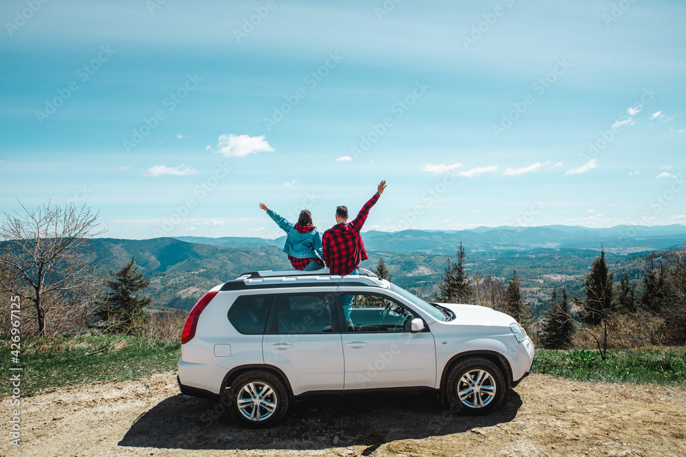 young woman sitting on the top of the suv car at mountain peak enjoying the landscape view