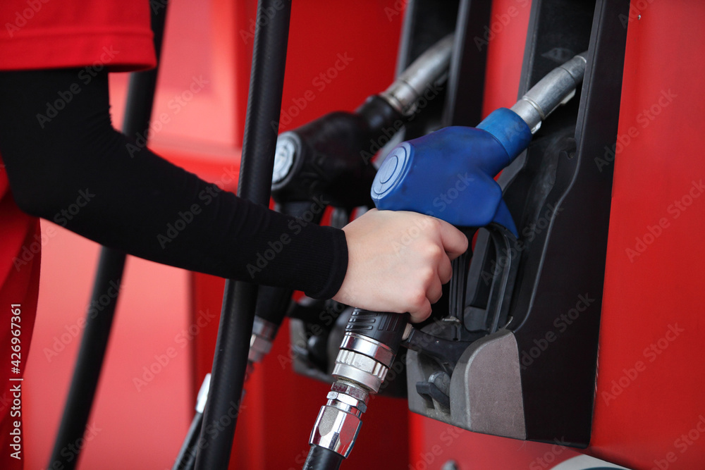 arm of woman with red uniform at the gas station for service , young woman refuel the car or Young girl with fuel pump nozzle at modern gas station arm of woman with red uniform at the gas station for service , young woman refuel the car or Young girl with fuel pump nozzle at modern gas station