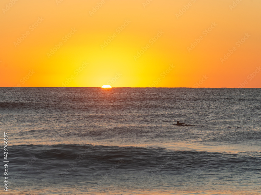 Silhouette of Surfer Swimming to the Sunrise. Narrabeen, Sydney, Australia.