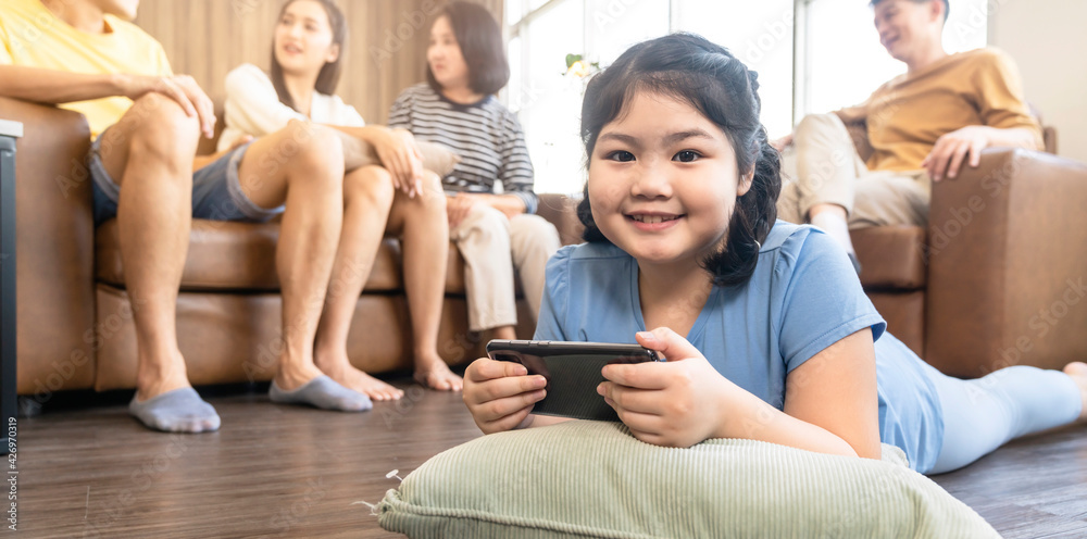 Fototapeta premium asian daughter child concentrate focus hand use smartphone game online playing with cheerful and fun quarantine stay home in living room home interior background