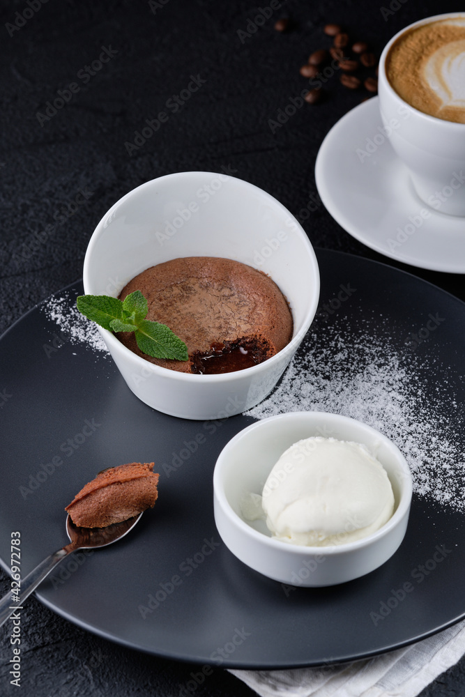 Chocolate brownie and ice cream on a dark grey plate next to a cup of coffee. View from above. Chocolate brownie and ice cream on a dark grey plate next to a cup of coffee. View from above.