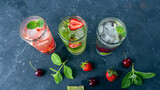 Three glass of refreshing cool detox drink with strawberry, lime, cherry and mint on dark background. Various summer lemonades or ice tea. Mojito cocktails with ice cubes. Healthy eating. Top view.