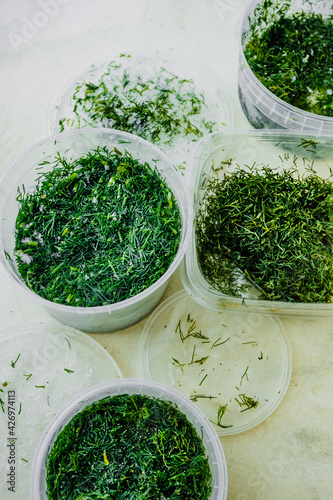 frozen fresh green dill in a plastic container. freeze food to keep it fresh. reasonable storage of products. food supplies. selective focus