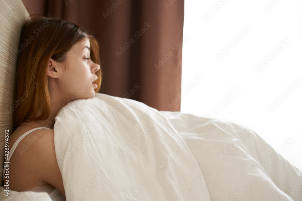 a pretty woman in a night suit is lying in bed under a blanket near the window on a weekend vacation a pretty woman in a night suit is lying in bed under a blanket near the window on a weekend vacation