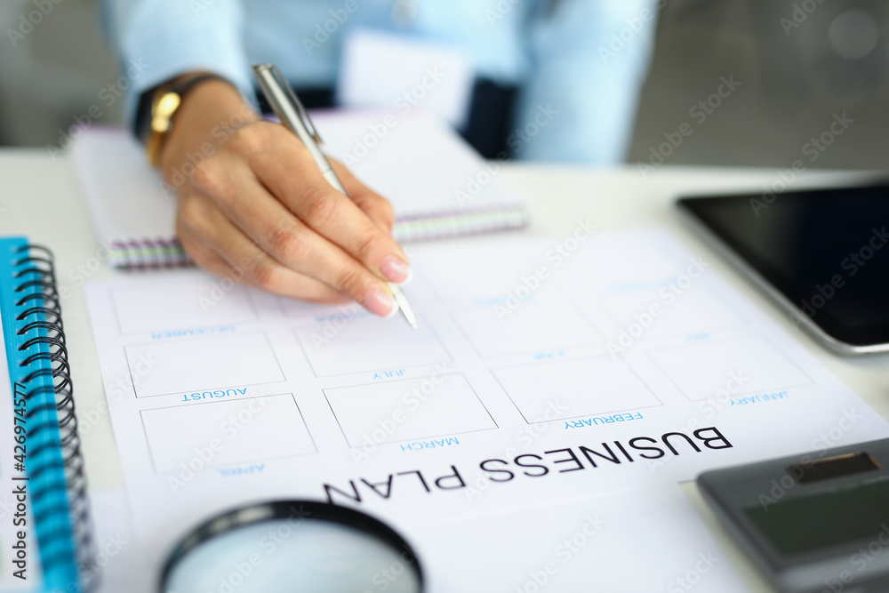 Woman hand holds pen and analyzes business plan Woman hand holds pen and analyzes business plan