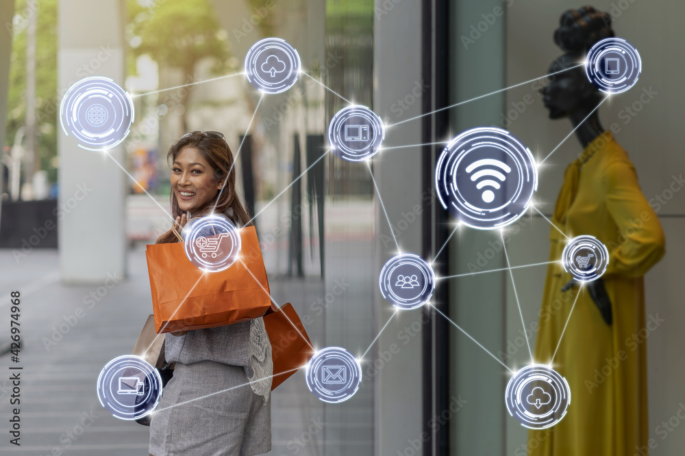 Wireless communication connecting of smart city Internet of Things Technology over Asian woman walking and looking through the glassess into the clothes on model display mockup in store shop