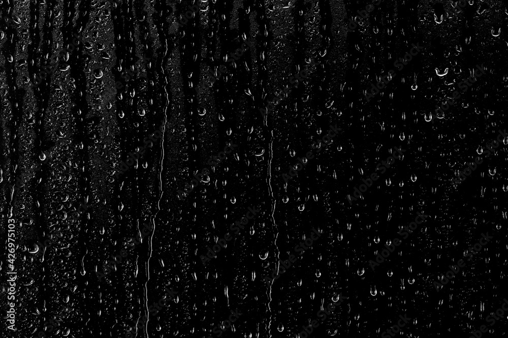 Drops of water flow down the surface of the clear glass on a black background. Texture for creativity.