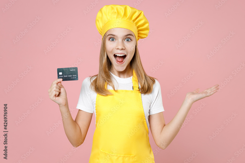 Teen shock girl chef cook confectioner housewife mother's helper baker in yellow apron white tshirt cap hold credit bank card spread hand isolated on pink background studio portrait Food cake concept Teen shock girl chef cook confectioner housewife mother's helper baker in yellow apron white tshirt cap hold credit bank card spread hand isolated on pink background studio portrait Food cake concept