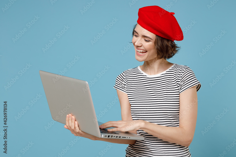 Young freelancer copywriter woman 20s with short hairdo wear french beret red hat striped tshirt hold laptop pc computer chat online browsing search isolated on pastel blue background studio portrait Young freelancer copywriter woman 20s with short hairdo wear french beret red hat striped tshirt hold laptop pc computer chat online browsing search isolated on pastel blue background studio portrait