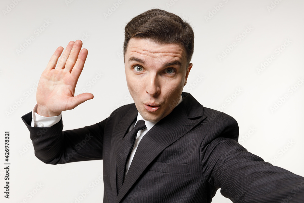 Close up young employee business corporate lawyer man in classic formal black grey suit shirt tie work in office do selfie shot mobile phone waving arm greet hello isolated on white background studio Close up young employee business corporate lawyer man in classic formal black grey suit shirt tie work in office do selfie shot mobile phone waving arm greet hello isolated on white background studio