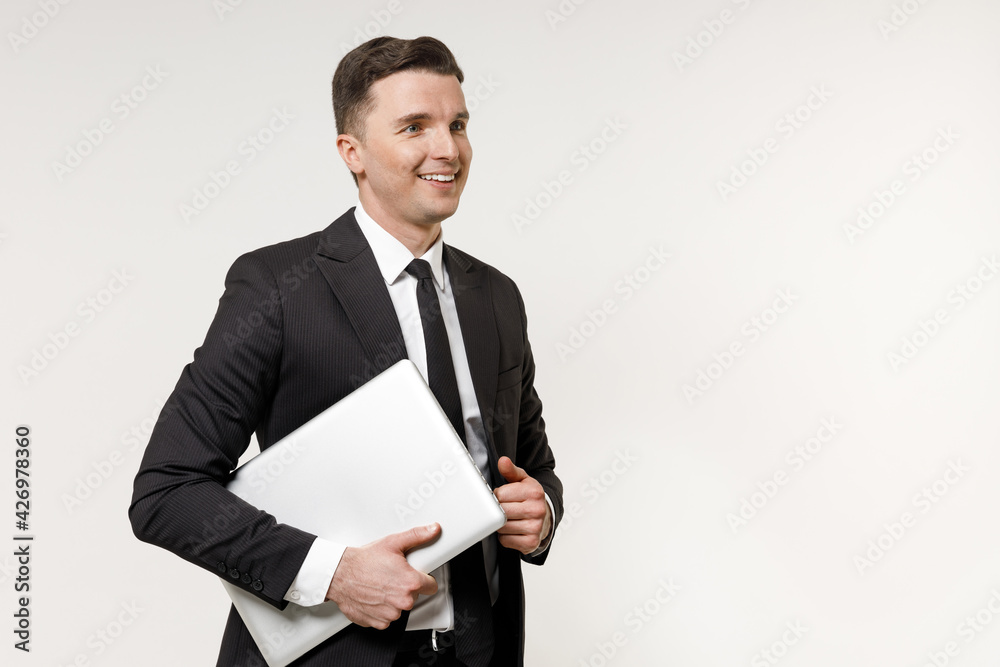 Young employee business corporate lawyer man in classic formal black grey suit shirt tie work in office hold closed walk look aside aptop pc computer isolated on white background studio portrait. Young employee business corporate lawyer man in classic formal black grey suit shirt tie work in office hold closed walk look aside aptop pc computer isolated on white background studio portrait.