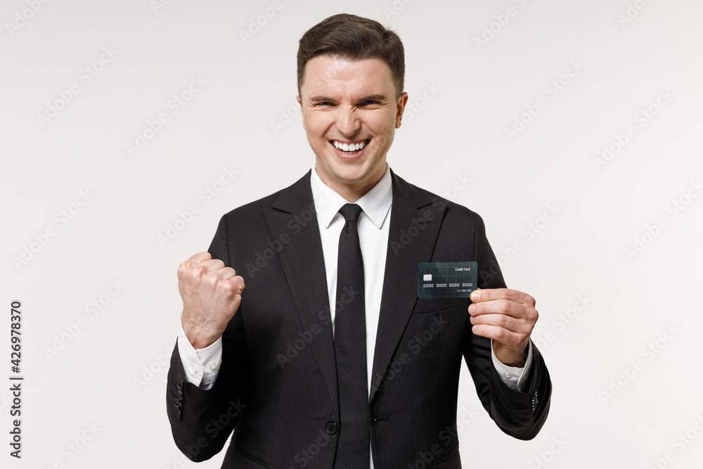 Young overjoyed successful rich employee business corporate lawyer man in classic formal black grey suit shirt tie work in office hold credit bank card do winner gesture isolated on white background. Young overjoyed successful rich employee business corporate lawyer man in classic formal black grey suit shirt tie work in office hold credit bank card do winner gesture isolated on white background.