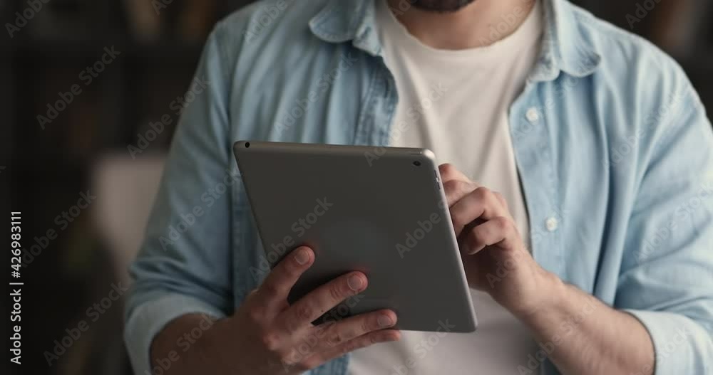 Close up young man holding digital computer touchscreen pad gadget in hands, web surfing information, shopping in internet store, using software applications, playing games or communicating distantly. Close up young man holding digital computer touchscreen pad gadget in hands, web surfing information, shopping in internet store, using software applications, playing games or communicating distantly.