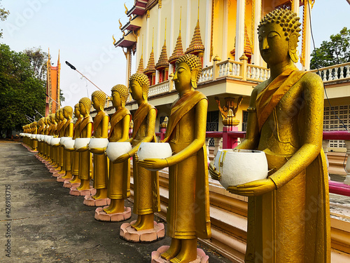 Golden statues of monks holding white alms bowl stand around the ordination hall