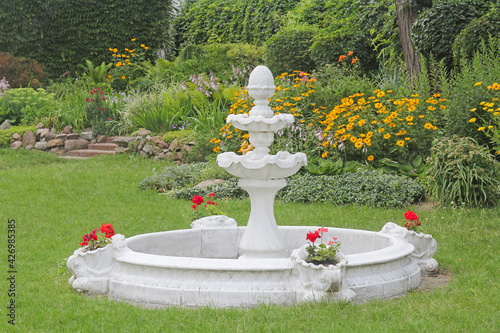 Decorative fountain on the lawn in the garden among flowers 