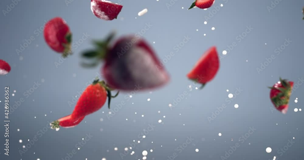SUPER SLOW MOTION shot of fresh sliced strawberries flying with yogurt or milk drops against blue background. Shot with high speed camera, 420 FPS