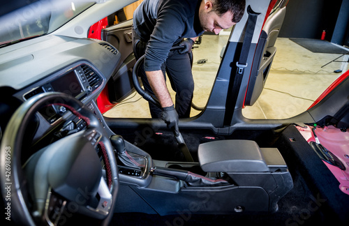 Car service worker cleaning car interior with a vacuum cleaner