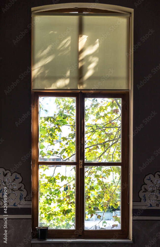 Close up interior shot of the window of a historical building with accompanying embroidery at wall. Foliage outside on a sunny day with dark interior. Close up interior shot of the window of a historical building with accompanying embroidery at wall. Foliage outside on a sunny day with dark interior.