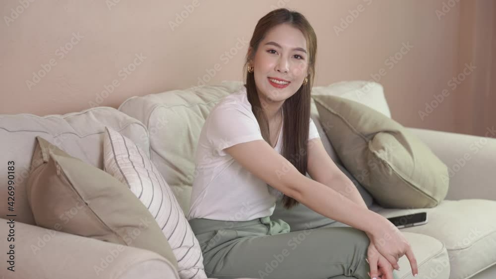 Woman charmingly while sitting on sofa. Happy young Asian girl smile for enjoys life Woman charmingly while sitting on sofa. Happy young Asian girl smile for enjoys life