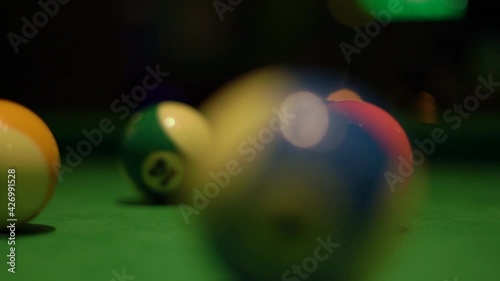 Motion past billiard balls with numbers lying on modern pool table covered with green velvet fabric in semi-dark bar hall extreme closeup.