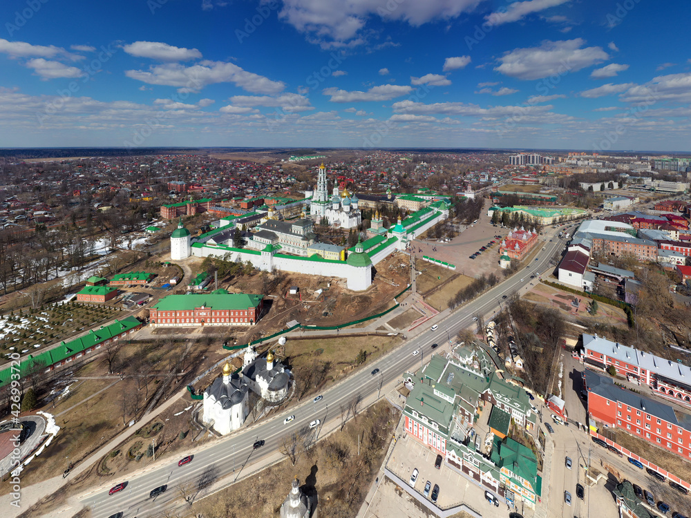 Fototapeta premium a panoramic view of the golden towers and ancient architectural solutions of the Trinity-Sergius Lavra in Sergiev Posad on a sunny spring day filmed from a drone 