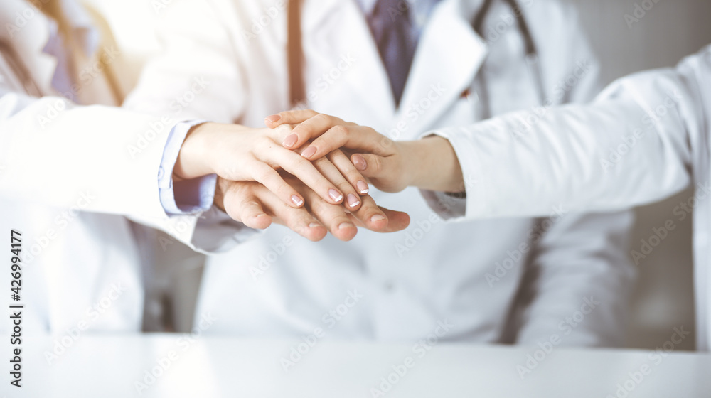 Fototapeta premium Group of modern doctors joining hands as a circle. Teamwork in medicine during Coronavirus pandemic, covid 2019