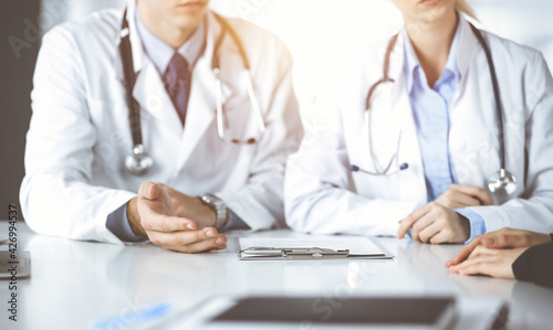 Unknown woman-doctor with male colleague are consulting patient woman while sitting at the desk in sunny clinic, close-up. Covid 2019