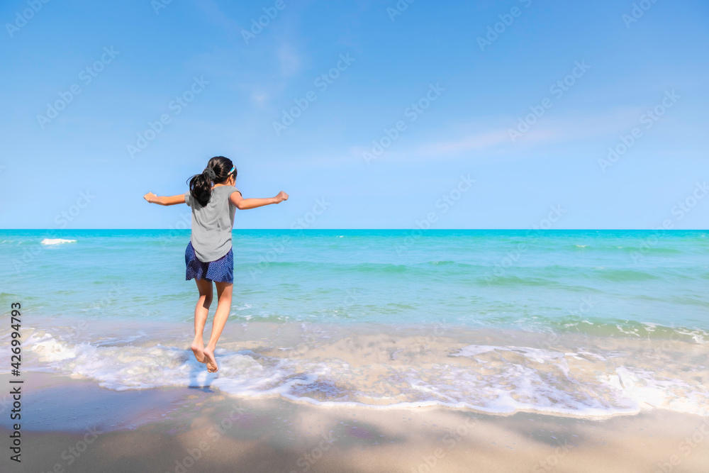 Asian kid girl jump playing jump on the beach with turquoise blue sea Asian kid girl jump playing jump on the beach with turquoise blue sea