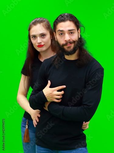 Young woman and man smiling cheerfully stand on the green chroma key background. There is a blank space for advertising content on the guy's tshirt's. Brand's position. Relationships. Pretty couple. 