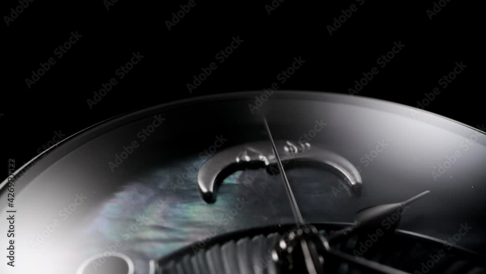 Silver second arrow running on nacrous clockface of rotating swiss made watch with smiling moon. Closeup of metallic details and ribbed pattern on black background Silver second arrow running on nacrous clockface of rotating swiss made watch with smiling moon. Closeup of metallic details and ribbed pattern on black background