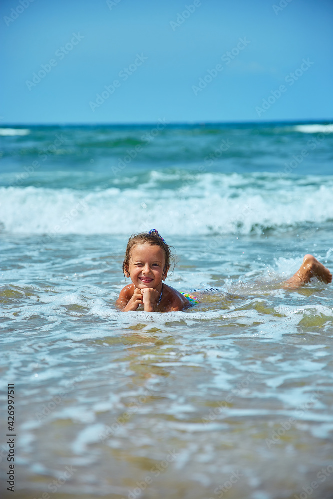 Happy little girl lies on the seashore in the waves