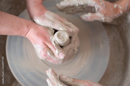 Women working on the potter's wheel. Hands of teacher show to student how to hold and push clay. Girl sculpt cup from white clay pot. Workshop on modeling do plate. Concept: handmade, workshop, artist