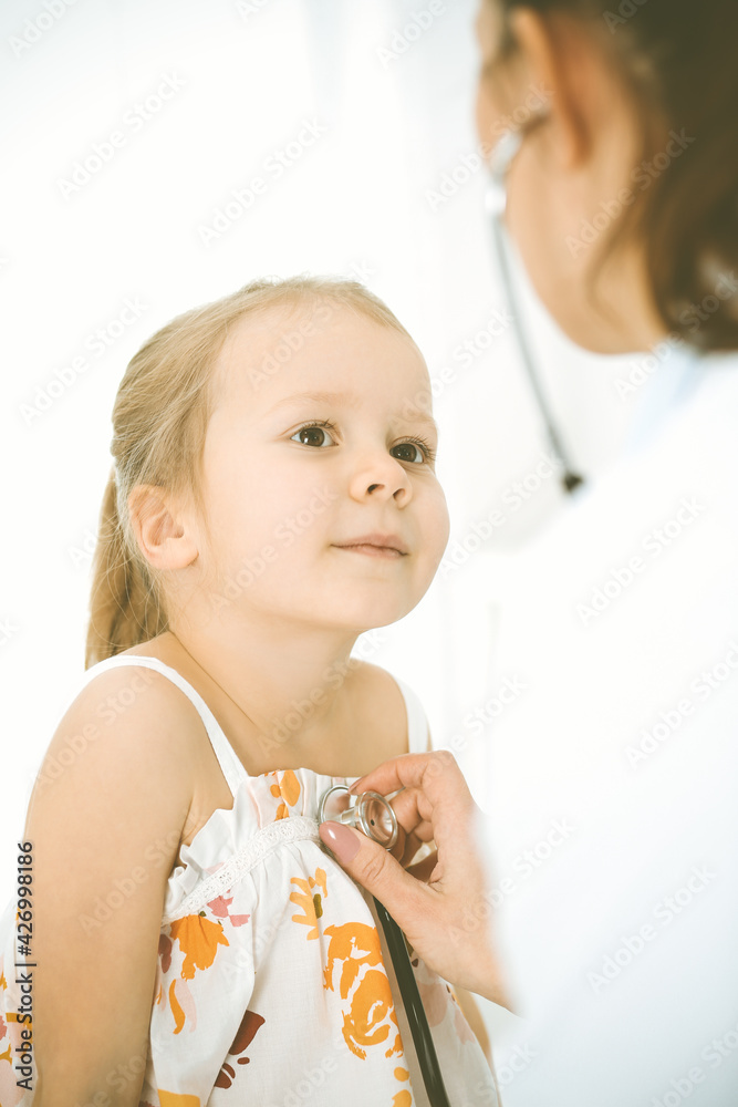Doctor examining a child by stethoscope. Happy smiling girl patient dressed in bright color dress is at usual medical inspection Doctor examining a child by stethoscope. Happy smiling girl patient dressed in bright color dress is at usual medical inspection