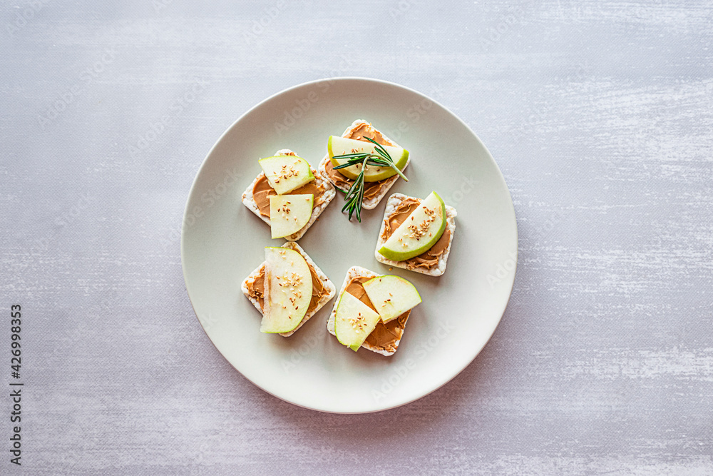 Healthy breakfast with peanut butter and apple sandwiches on rice cakes. Top view on grey concrete background, copy space.