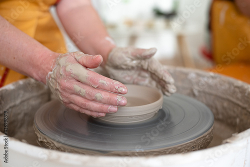 Woman working on potter's wheel, makes cup. Hands sculpt cup from white clay pot. Workshop on modeling do plate.  Concept: handmade, workshop, artist. Close-up.