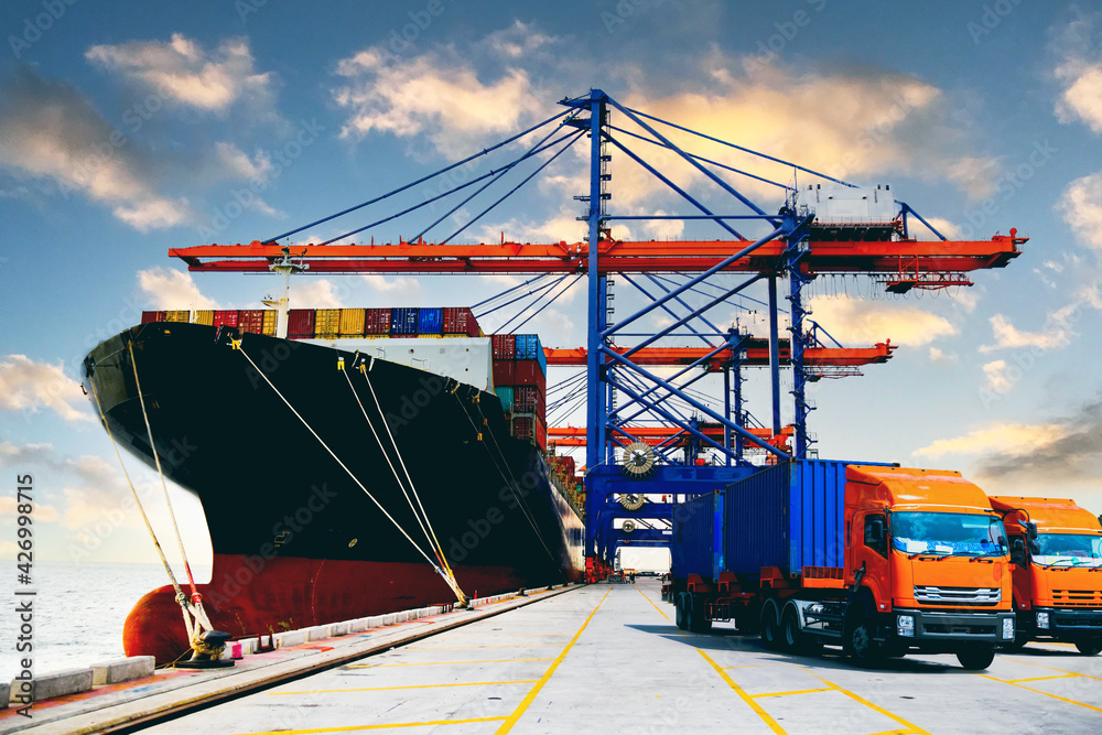 Fleet of heavy duty trucks receive cargo container from huge ship under quay crane. Container logistic import export and transport industry background. Fleet of heavy duty trucks receive cargo container from huge ship under quay crane. Container logistic import export and transport industry background.