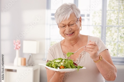 Photo Happy old lady eating fresh green salad, smiling.