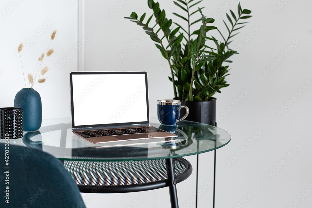 Laptop wiith white screen on wooden table in home scandi interior. Stylish minimalistick workplace, copy space