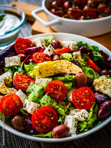 Fresh Greek salad - feta cheese, cherry tomatoes, artichokes, lettuce, black olives and onion on wooden table 