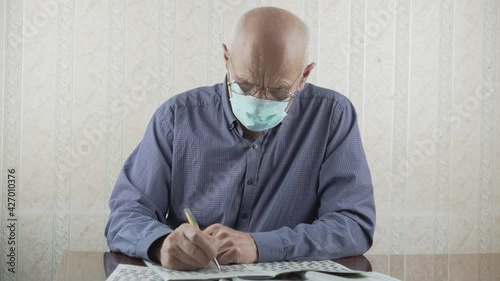Elderly bald person in protective face mask sloving crossword with pen photo
