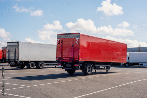 Trucks and trailers on a parking lot in front of a distribution center. Red and White trailers without writing.