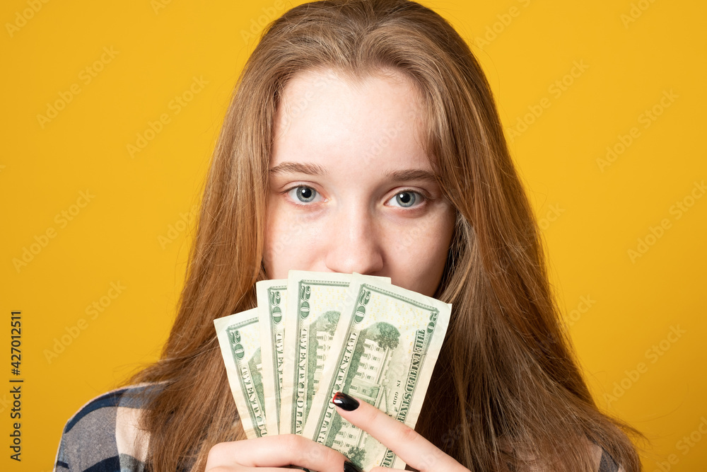 Close up portrait of a young girl holding money on a yellow background. Close up portrait of a young girl holding money on a yellow background.
