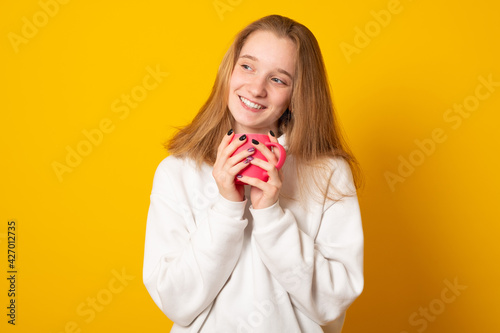 Cute teen girl wearing a white hoodie warms on a hot cup of tea. Young girl in autumn hoodie drinking from a colorful mug.