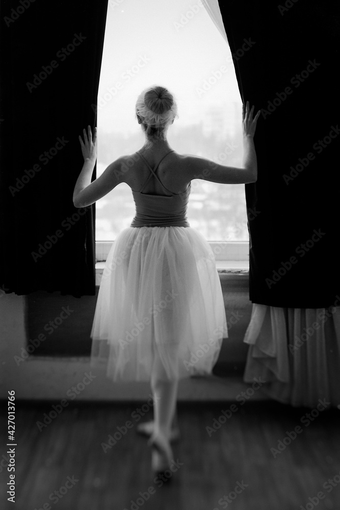 Young and graceful ballerina in pointe shoes and a black dress dancing in the studio. Choreography and dancing classes concept. Creative ideas of ballet posing, performance. 