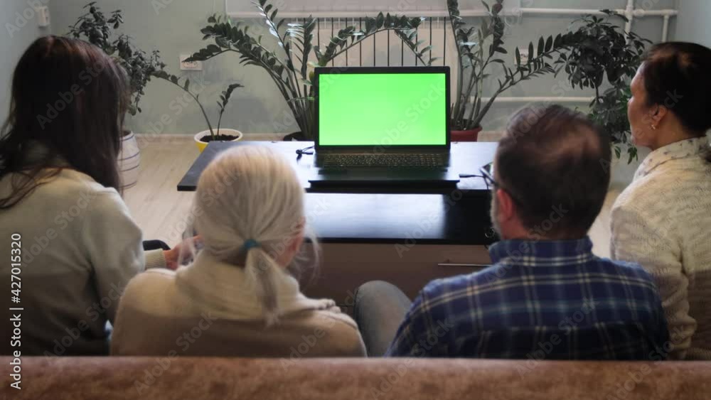Family watching laptop. Green screen. A family of four is sitting on the couch. In front of them is a laptop with a green screen. Grandma points her finger at the screen. Family watching laptop. Green screen. A family of four is sitting on the couch. In front of them is a laptop with a green screen. Grandma points her finger at the screen.