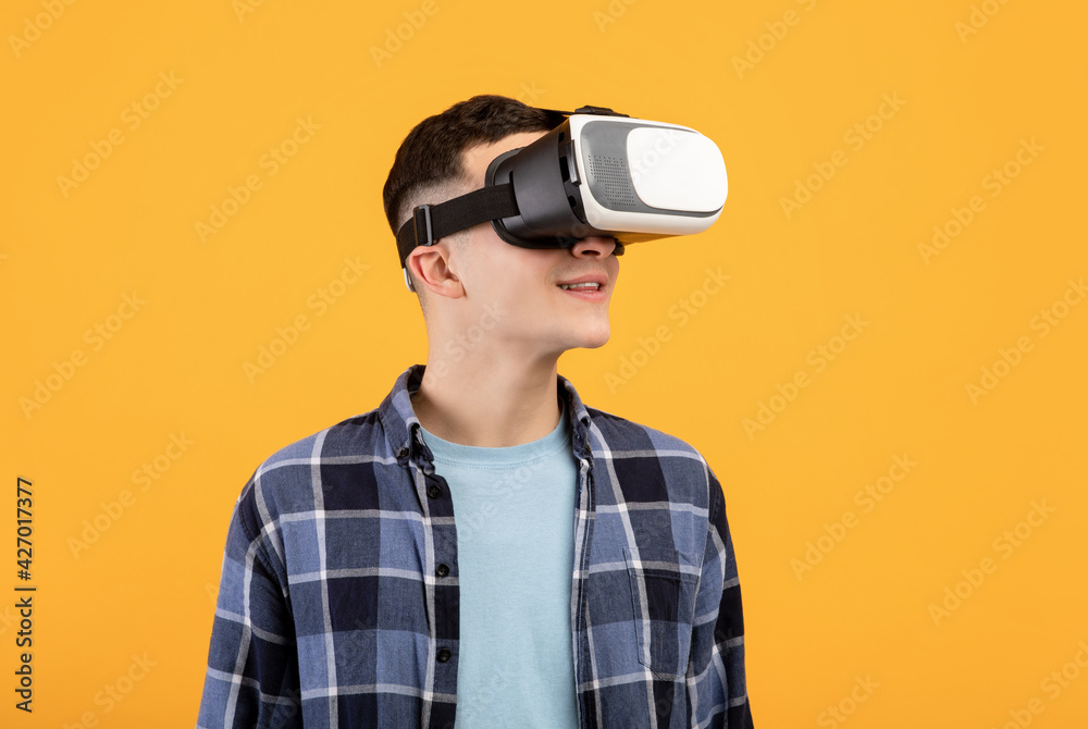 Cool guy in VR headset exploring cyberspace, using virtual reality for entertainment or studies on orange background Cool guy in VR headset exploring cyberspace, using virtual reality for entertainment or studies on orange background